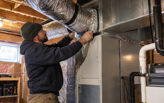 Installer sealing insulated ductwork to a central heat pump air handler in a basement